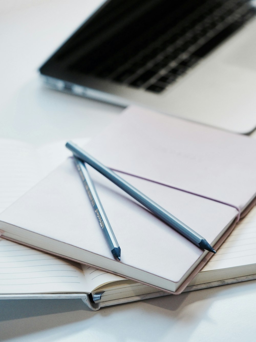 close-up photography of two pencils on closed pink covered book on desk near MacBook Air in a well-lit room