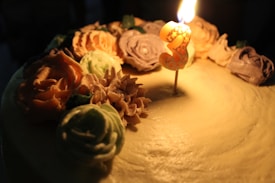 A birthday cake decorated with intricate frosting flowers surrounding a lit number three candle.