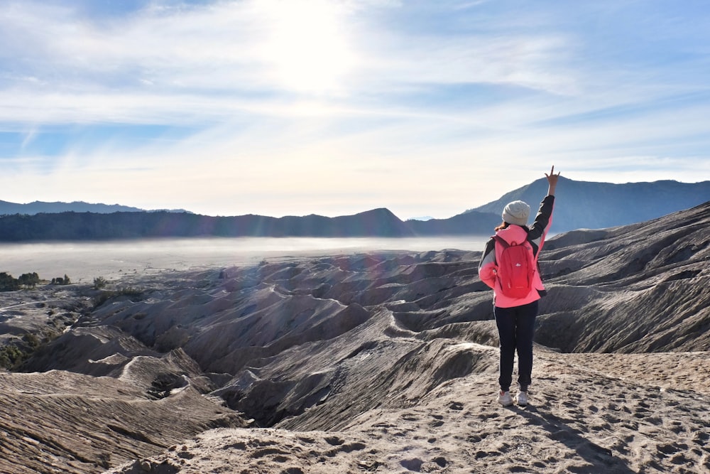 woman raising right hand facing mountain under cloudy sky