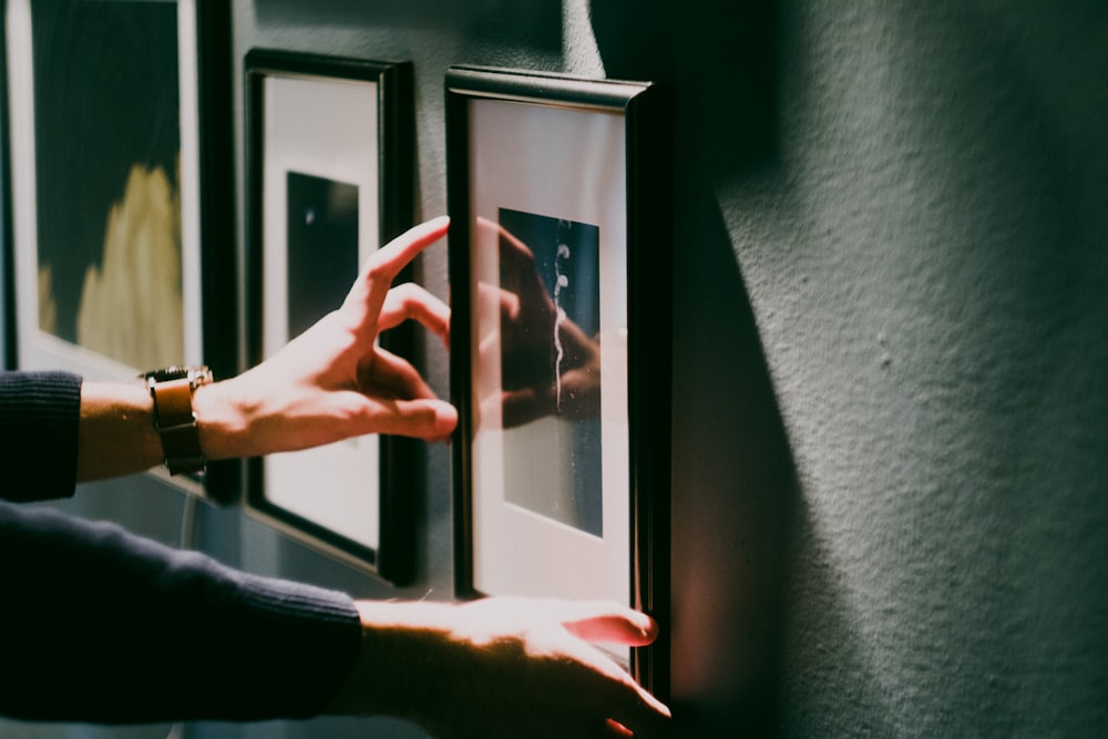 person aligning framed decor on gray wall