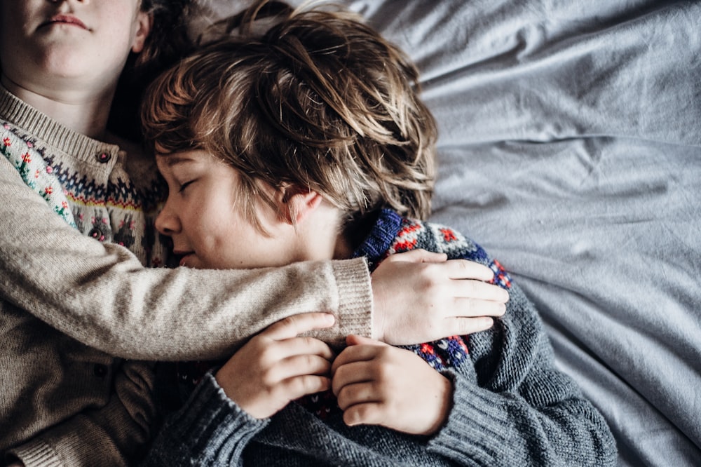 Niña y niño acostados en la cama con sudaderas marrones y grises