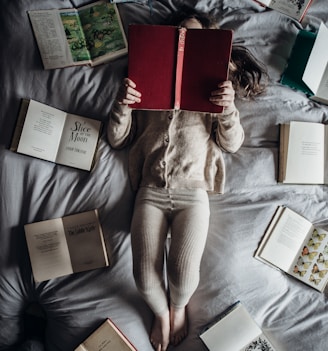 a little girl laying on a bed with lots of books