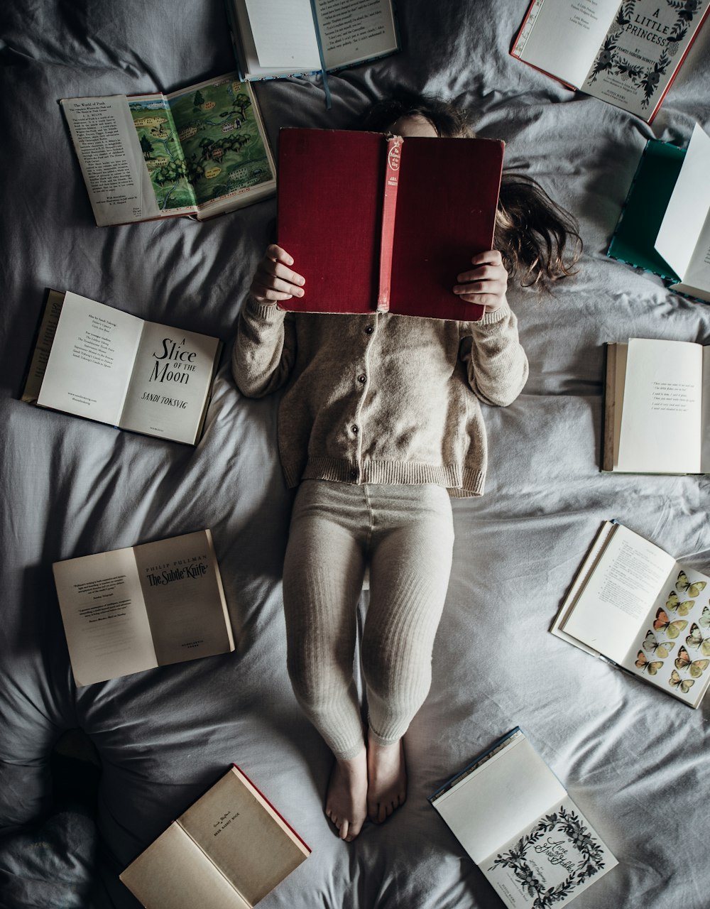 a little girl laying on a bed with lots of books