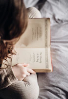 A smiling woman wearing a cozy Vorzaya sweater, enjoying a quiet moment with a book.
