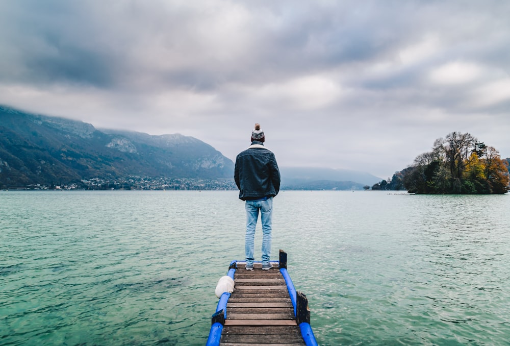 man standing on edge of dock facing mountains