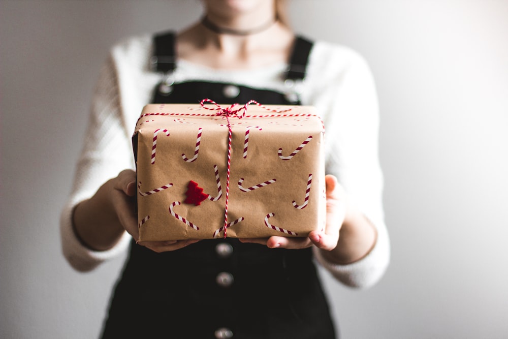 Fotografía de lente de cambio de inclinación de mujer sosteniendo una caja de regalo con impresión de bastón de caramelo en una habitación bien iluminada