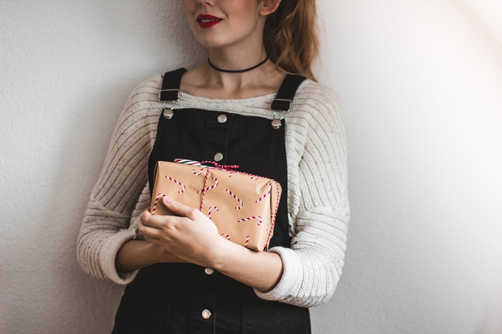 woman carrying brown leather bag while standing near white painted wall