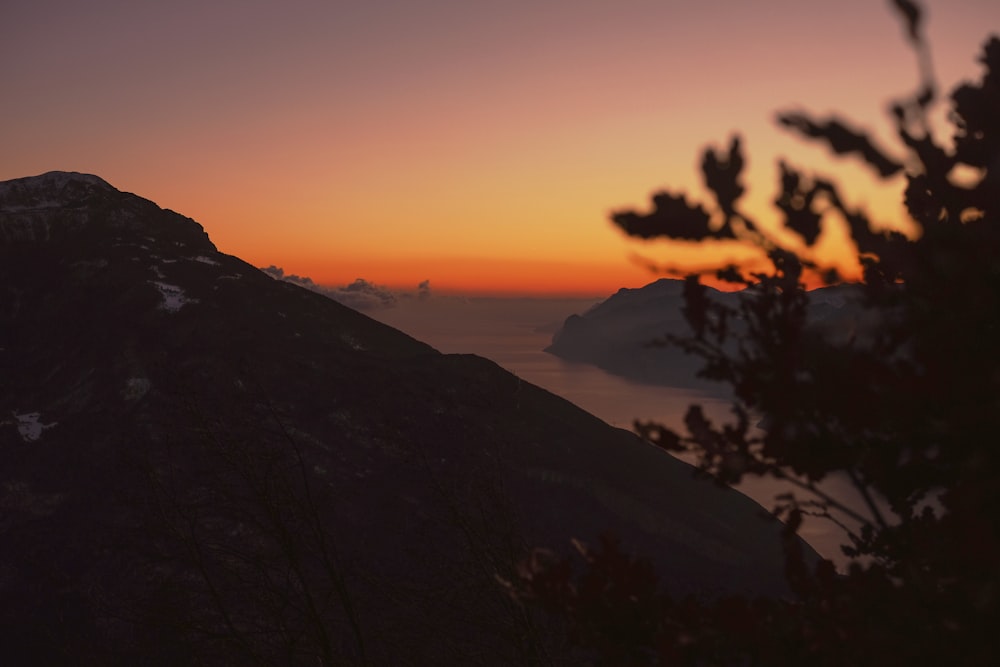 high-angle silhouette photography of mountain ranges with body of water in between during golden hour