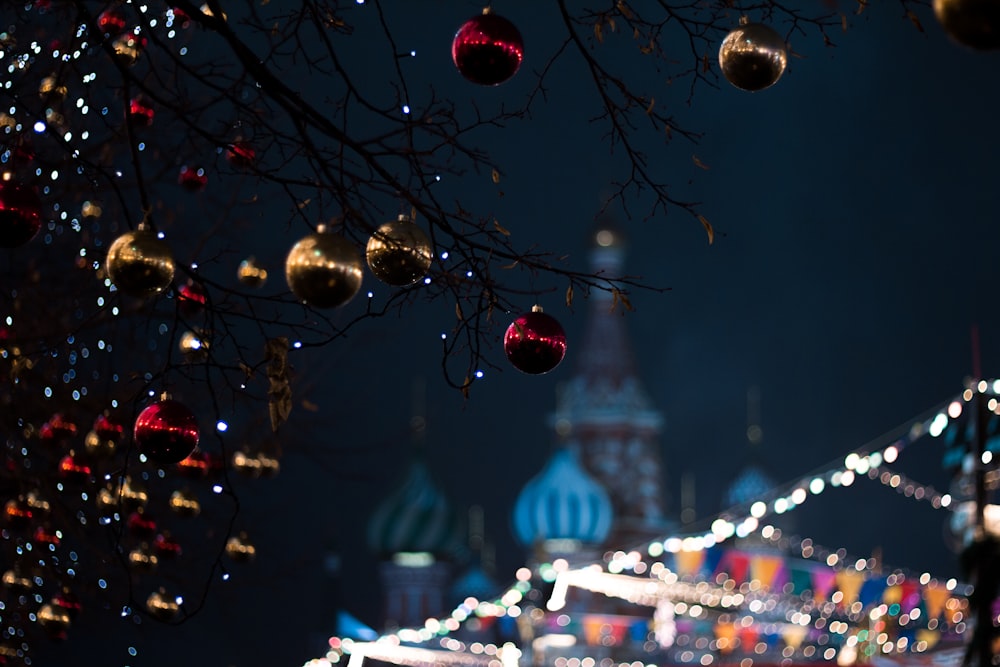 rote und braune Weihnachtskugeln, die nachts an Bäumen in der Nähe von beleuchteten Gebäuden hängen