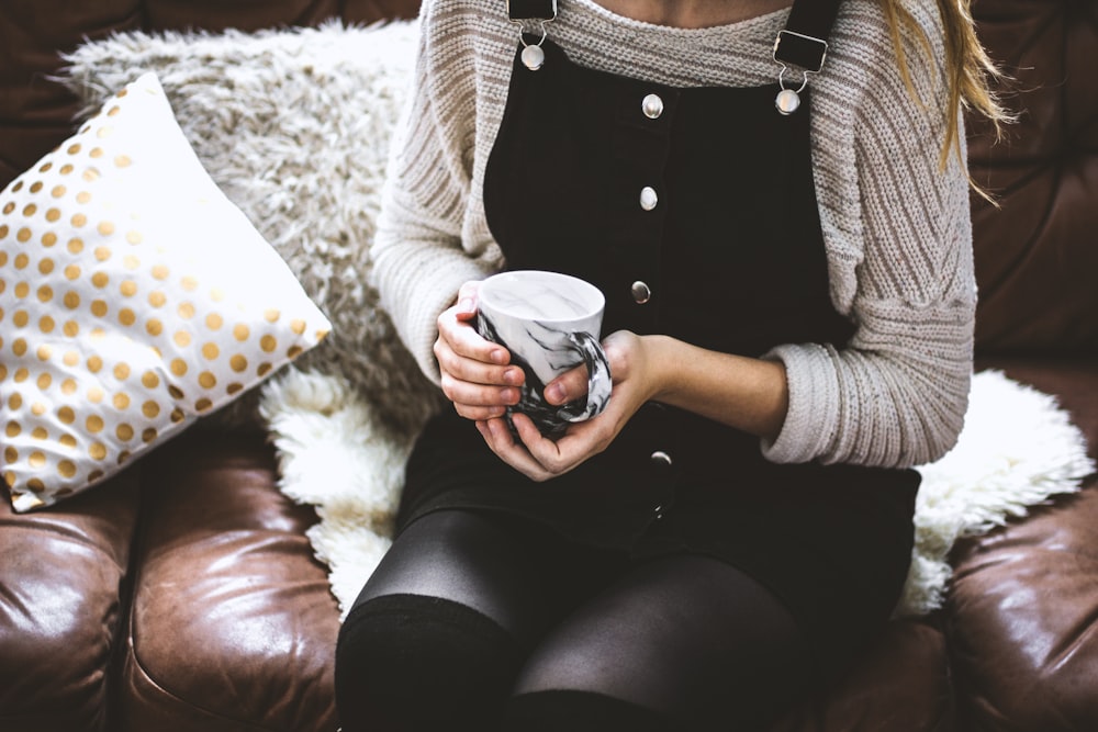 woman sitting on the sofa holding white and black ceramic mug