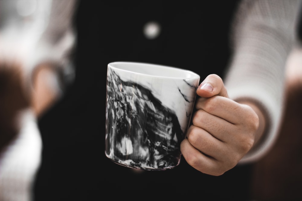 person holding a white and black ceramic mug