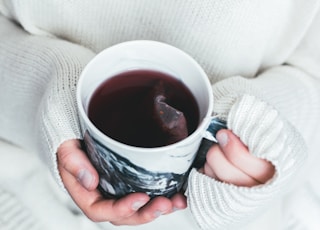 person holding white and black cup with teabag inside