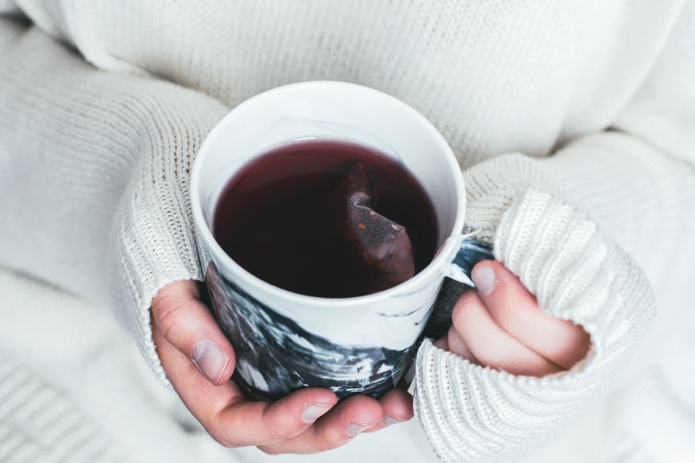 persona sosteniendo una taza blanca y negra con bolsita de té en el interior