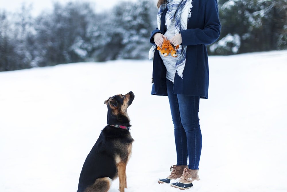 woman standing beside black dog on snow field