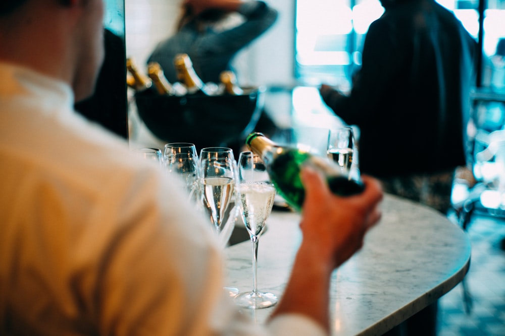 personne portant une chemise tenant une bouteille de vin versant sur du verre pendant la photographie de jour