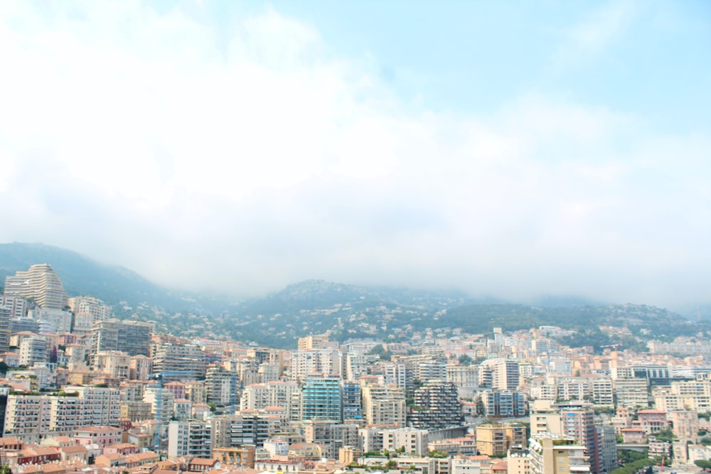 Foto del edificio de gran altura de la ciudad de colores variados cerca de las montañas verdes bajo el cielo nublado durante el día