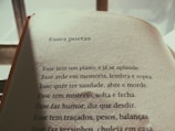 The image features an open book with a page of Portuguese text. The title reads 'Esses poetas,' followed by several poetic lines. The lighting is warm and casts a soft shadow on the page, suggesting early morning or late afternoon sunlight.