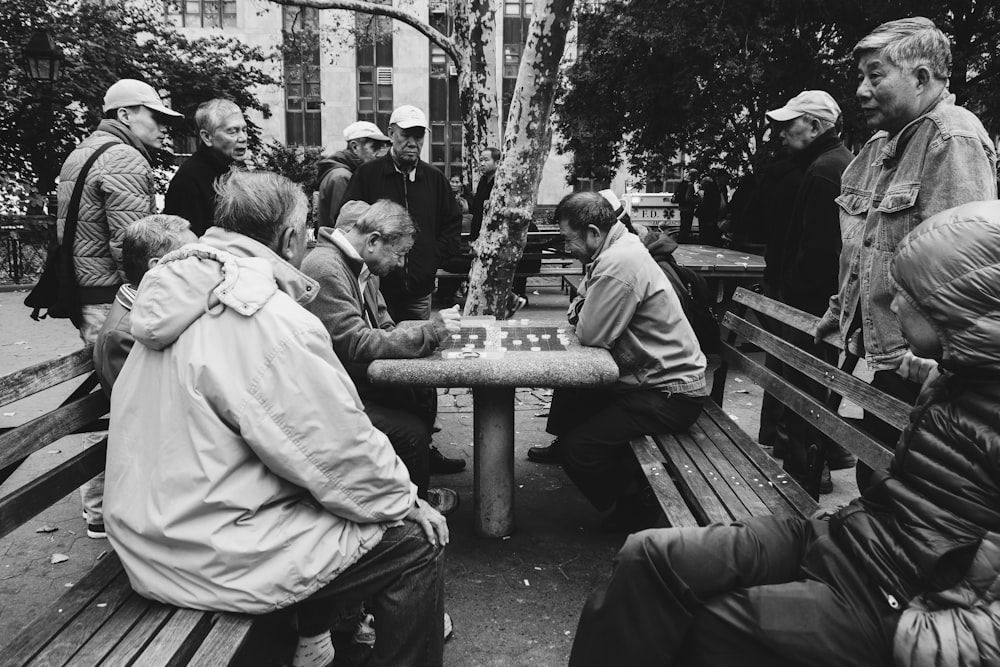 greyscale photo of people on park watching two people playing board game