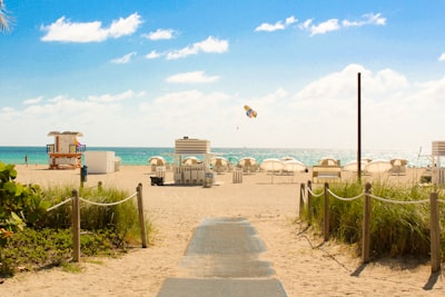 gray pathway leading to parasol, lifeguard house, and sea a daytime florida teams background