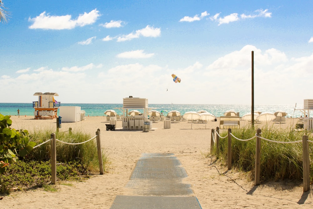 gray pathway leading to parasol, lifeguard house, and sea a daytime