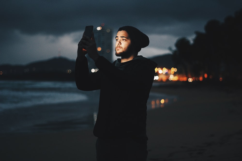 man using mobile phone on beach during dusk