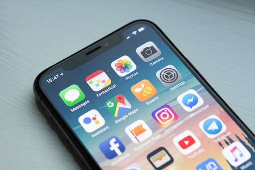 Close-up of a modern smartphone with a black frame displaying a variety of colorful application icons on the screen. The apps include Messages, Photos, Camera, and popular social media platforms such as Instagram and Facebook Messenger.