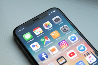 Close-up of a modern smartphone with a black frame displaying a variety of colorful application icons on the screen. The apps include Messages, Photos, Camera, and popular social media platforms such as Instagram and Facebook Messenger.