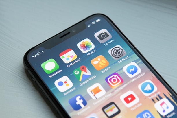 Close-up of a modern smartphone with a black frame displaying a variety of colorful application icons on the screen. The apps include Messages, Photos, Camera, and popular social media platforms such as Instagram and Facebook Messenger.