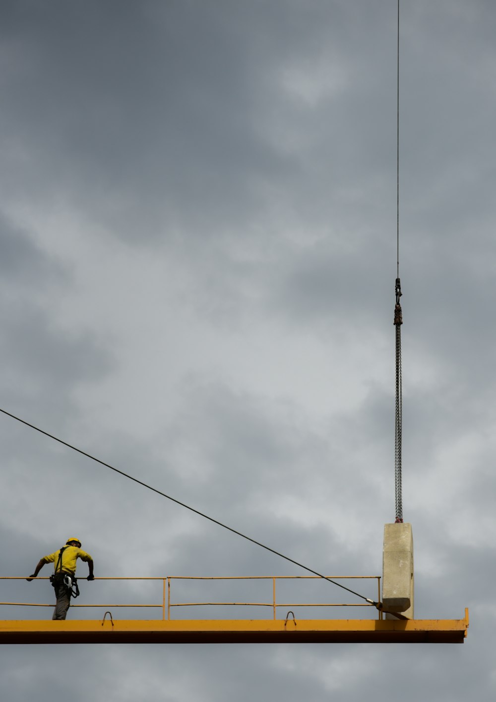 昼間の青い曇り空の下、黄色い金属製のプラットフォームの手すりを持つ黒いハーネスストラップを身に着けた男性
