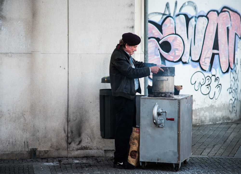 man holding gray cooking pot near wall graffiti during daytime