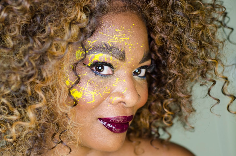 femme aux cheveux crépus souriant portant du rouge à lèvres rouge avec de la peinture jaune pour le visage