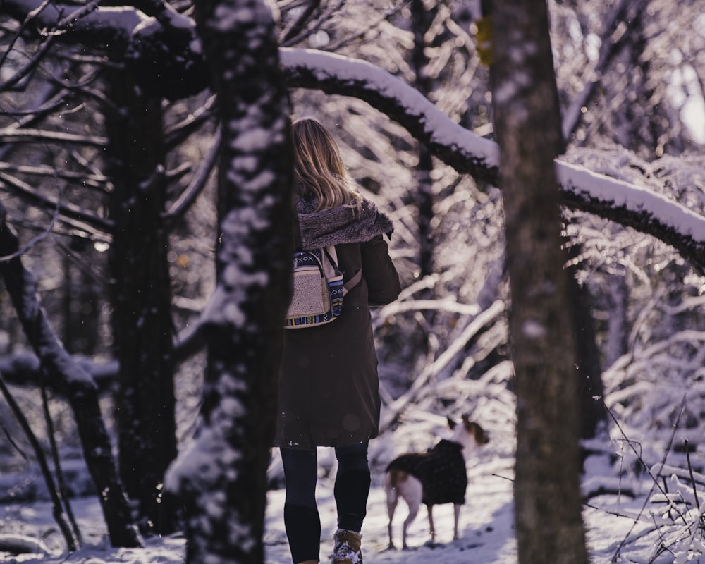 woman and dog standing on snow field near trees