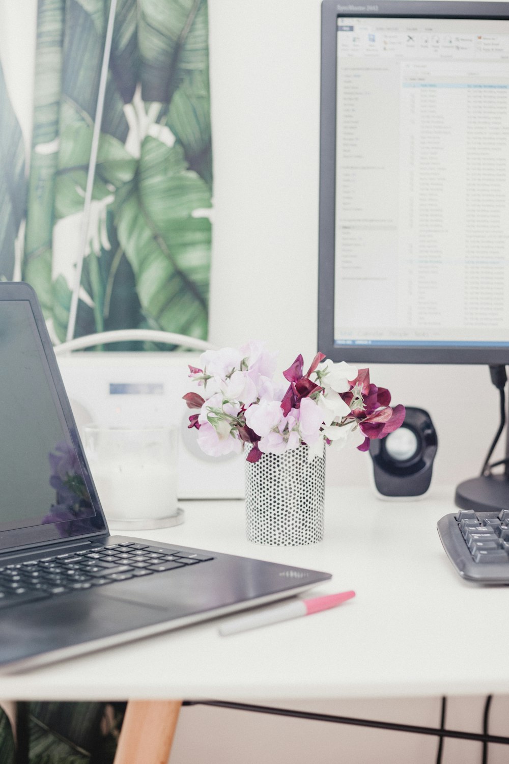 pink and red petaled flower on vase beside computers