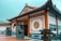 An ornate traditional Chinese building with intricate designs on the walls and roof. Two stone lion statues flank the entrance, which is open and adorned with elegant Chinese characters and geometric patterns. The surrounding area is well-maintained with plants and a tiled courtyard.