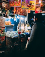 man with coat standing in front of food cart during nighttime