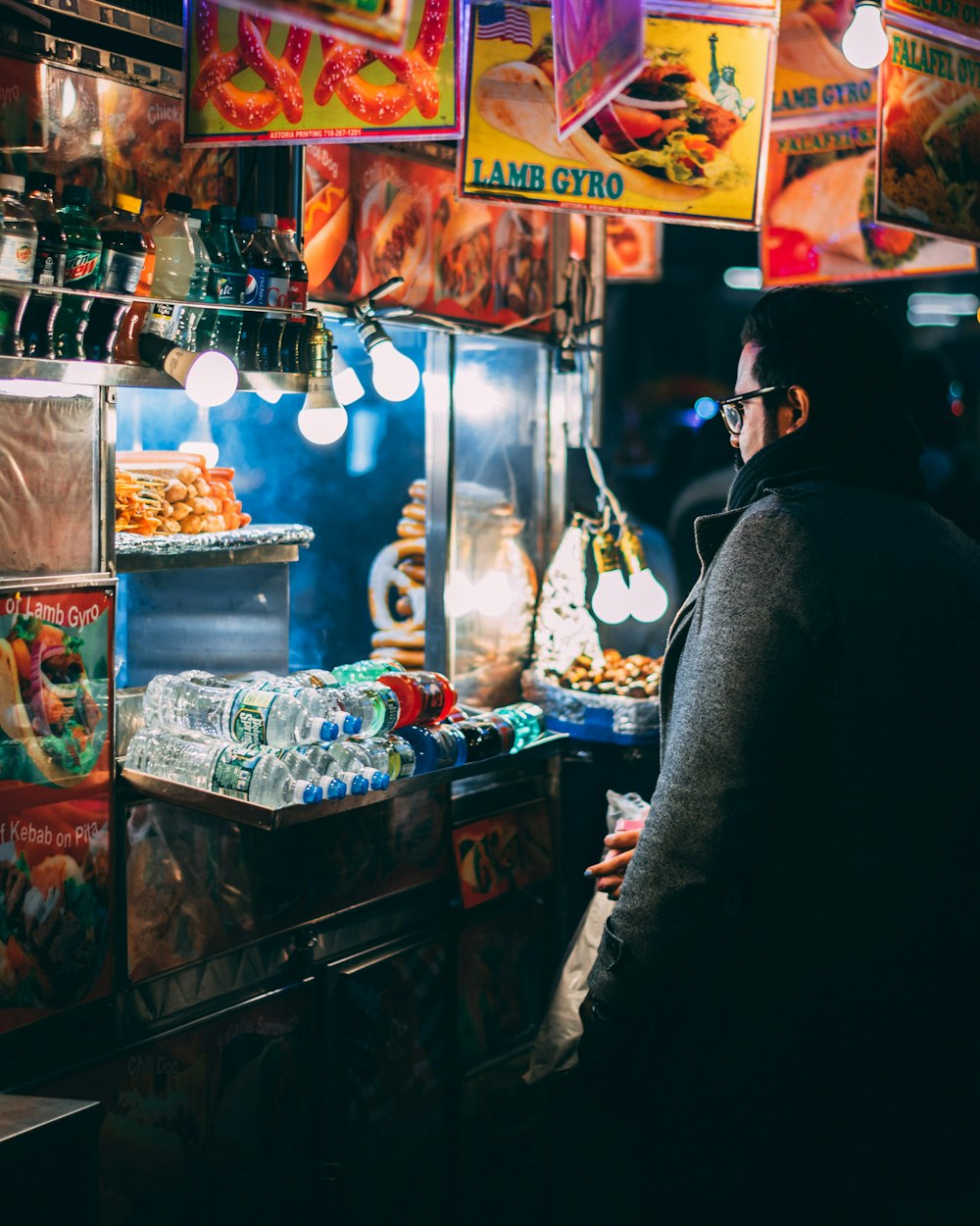 homme avec manteau debout devant le chariot de nourriture pendant la nuit