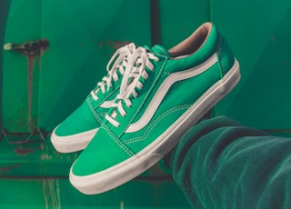 person holding pair of green Vans shoes