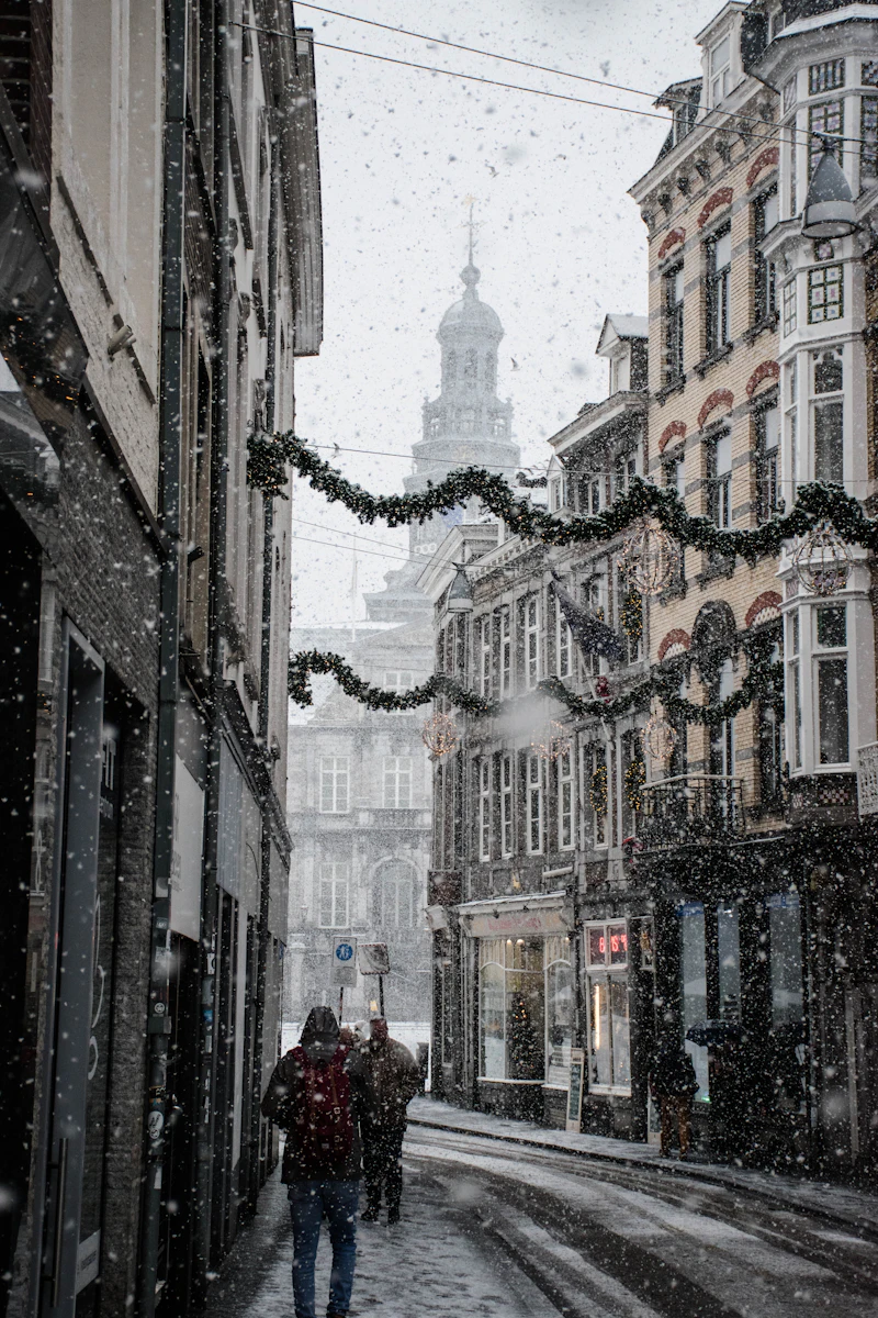 People walking a snow-covered street between old townhouses