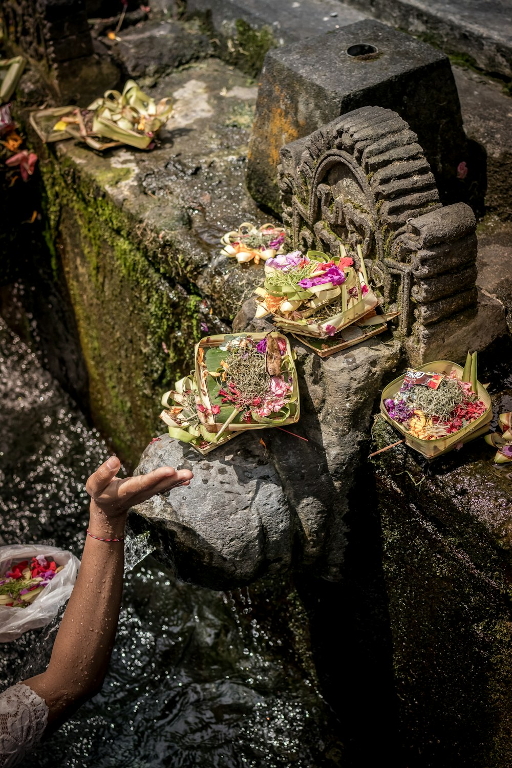 person's hand near concrete statuette with floral baskets at daytime