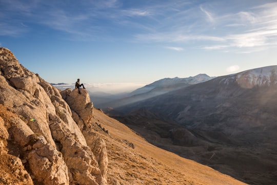man sitting of brown rock seeing mountains during daytime in Antalya Turkey