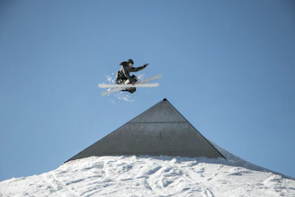 An action shot capturing a rider mid-air performing a stylish trick over a snow ramp.
