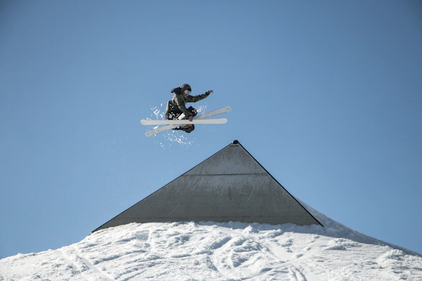 An action shot capturing a rider mid-air performing a stylish trick over a snow ramp.