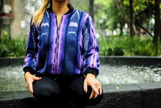 Woman wearing a purple and green gradient handmade jacket outdoors with sunlight highlighting textures.