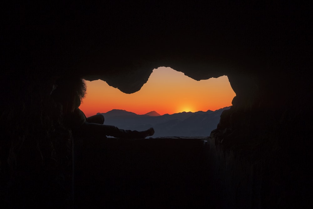 silhouette of person sitting on cave during golden hour