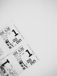 A close-up view of three movie tickets arranged in a layered fashion against a white background. The tickets are printed in black and white, featuring details such as the movie title 'Home Alone', showtime on December 9th at 11:00 AM, a pricing of $1.00, and a PG rating.