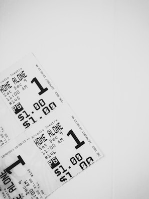 A close-up view of three movie tickets arranged in a layered fashion against a white background. The tickets are printed in black and white, featuring details such as the movie title 'Home Alone', showtime on December 9th at 11:00 AM, a pricing of $1.00, and a PG rating.
