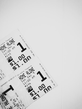 A close-up view of three movie tickets arranged in a layered fashion against a white background. The tickets are printed in black and white, featuring details such as the movie title 'Home Alone', showtime on December 9th at 11:00 AM, a pricing of $1.00, and a PG rating.