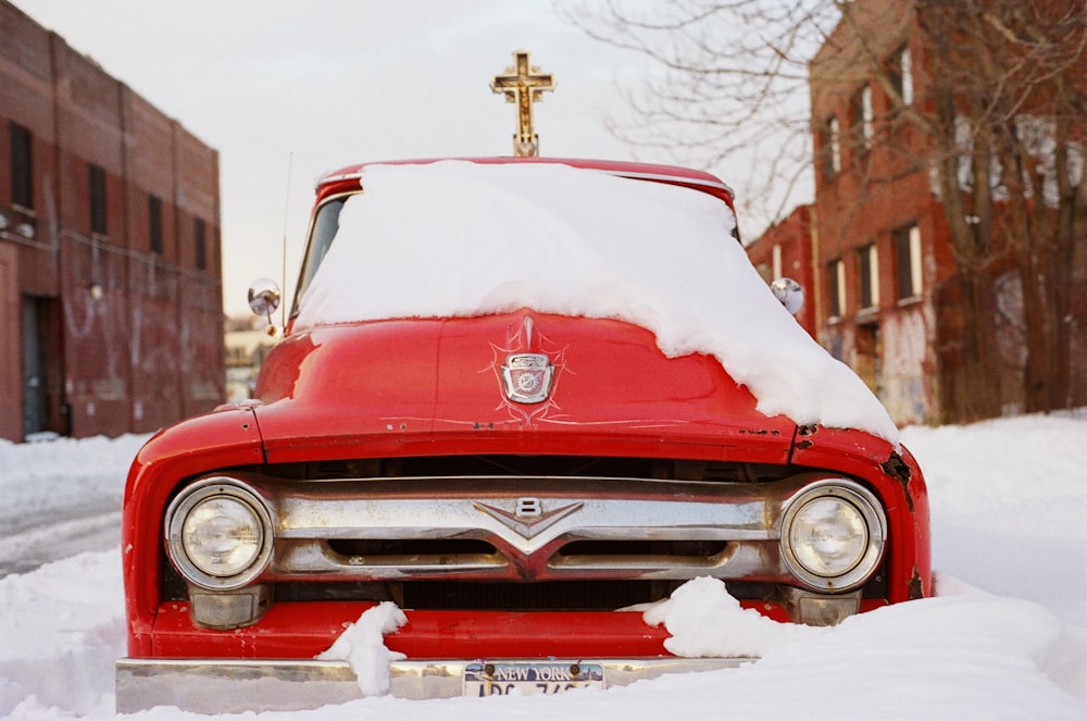 Vehículo rojo rodeado de un campo nevado junto a edificios de hormigón marrón durante el día