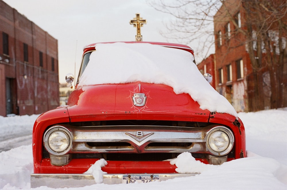 昼間、茶色のコンクリートの建物の横の雪原に囲まれた赤い車両