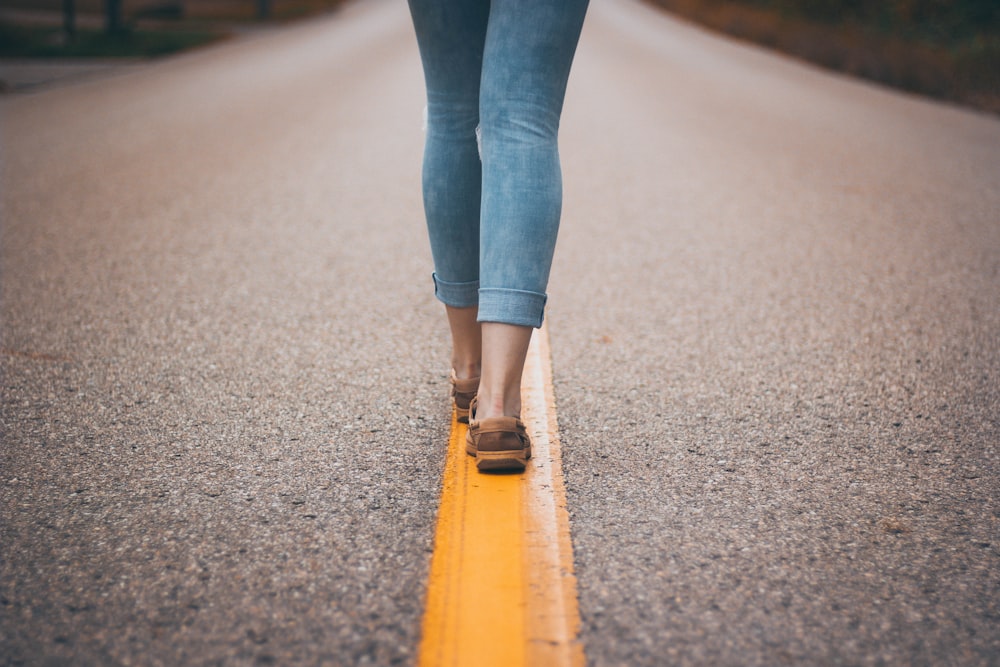 person wearing brown shoes standing on yellow line roadway during daytime